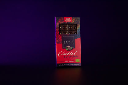 Eine einzelne Tafel der dunklen, zartbitteren Bio-Dattel-Schokolade mit einem Kakaoanteil von 85 Prozent in ihrer 70g Verpackung. Statt raffiniertem Zucker wurde sie ausschließlich mit natürlicher Dattelsüße gesüßt.