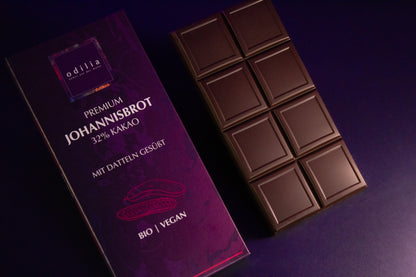 Die ausgepackte 70g Tafel der Premium Johannisbrot Schokolade liegt auf einer Unterlage, Fokus auf Schokolade und Johannisbrot.